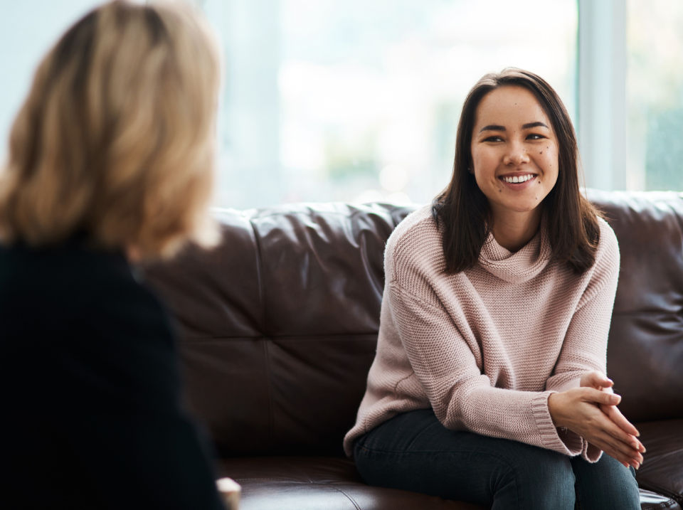 smiling woman sits on couch facing her counsellor