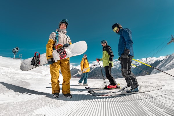 Group of six skiers and snowboarders standing with their gear on a ski run