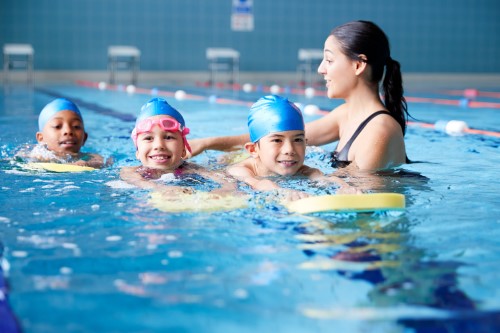 Children swimming pool while an adult helps them