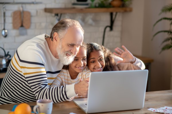 Man and two children smile and wave at a laptop screen