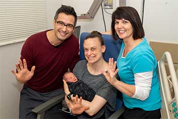 Smiling parents with newborn baby, and a hearing screening professional