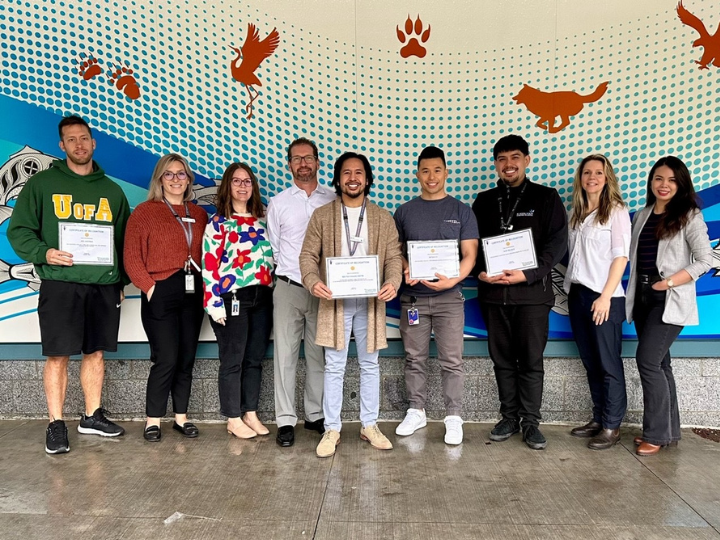 Nine smiling people holding award certificates